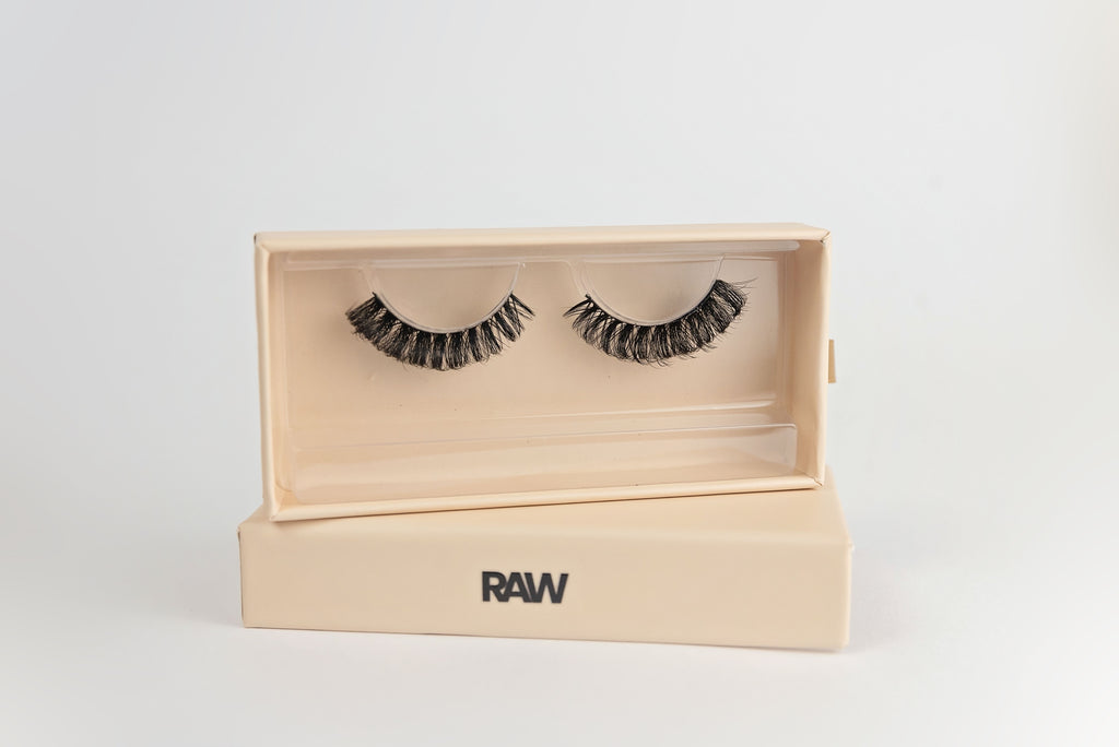 False eyelashes in an open wooden box with 'RAW' branding on a light gray background