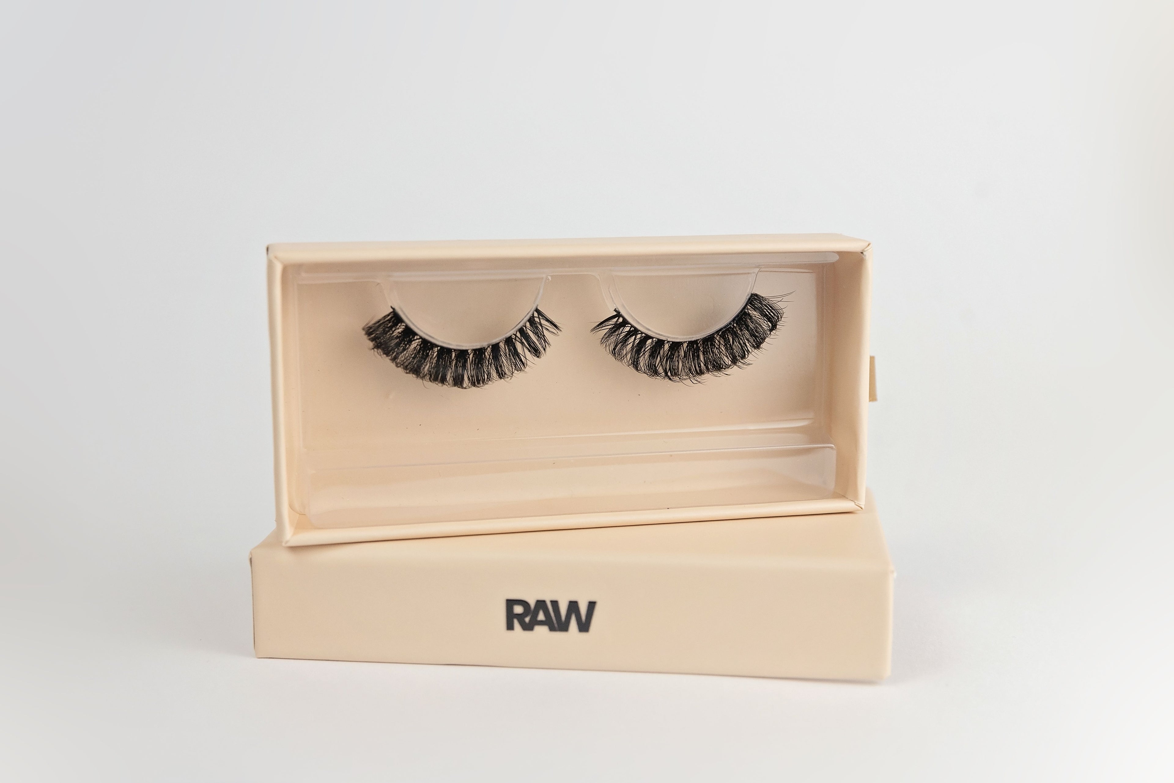 False eyelashes in an open wooden box with 'RAW' branding on a light gray background
